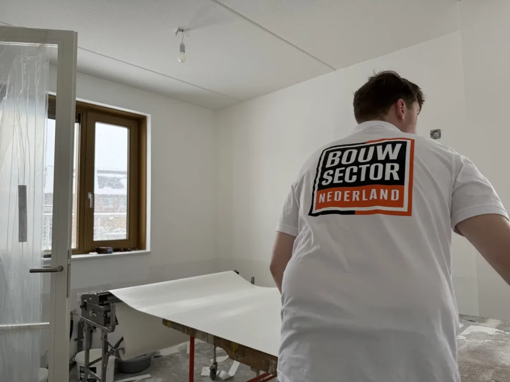 Behanger bij de plaktafel met een baan renovlies in een nieuwbouwkamer met een afgeplakte deur