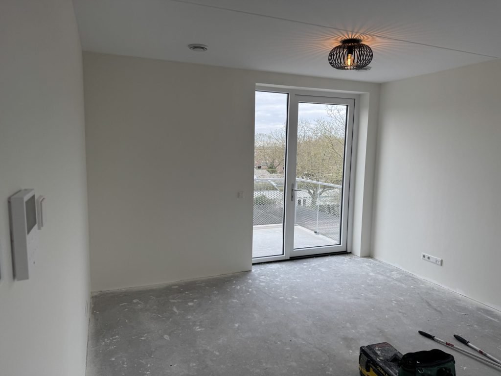 Lege kamer in een nieuw appartement met witte wanden, een betonvloer en een deur naar het balkon