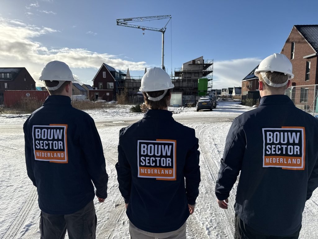 Drie behangers van Bouwsector Nederland in werkjas en bouwhelm tussen nieuwe huizen in aanbouw