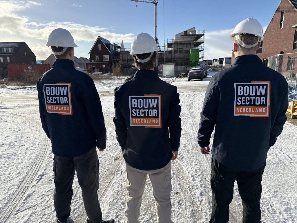 Drie vakmensen van Bouwsector Nederland met bouwhelm op een besneeuwde nieuwbouwlocatie met een bouwkraan